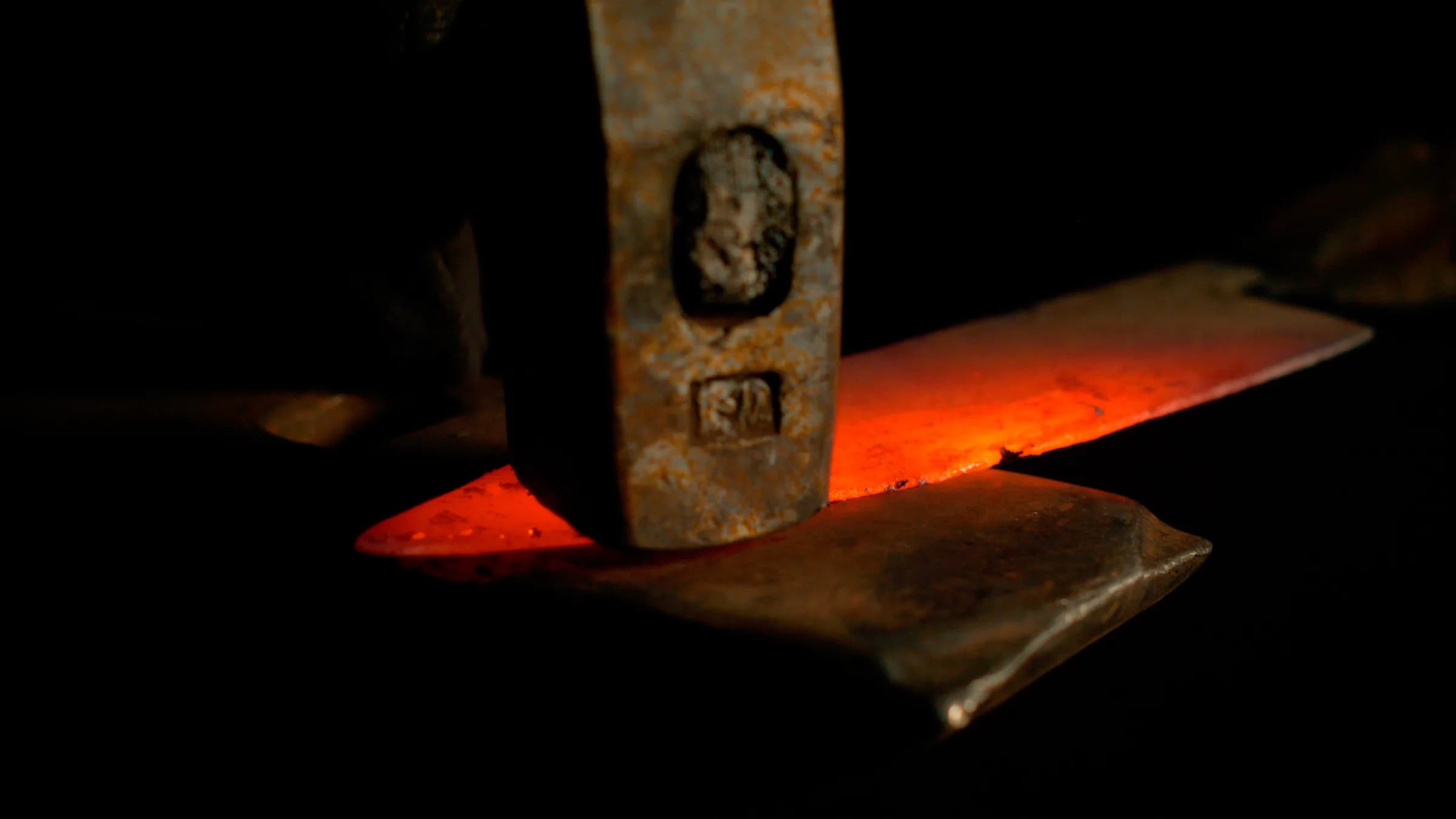 Hot steel held by tongs, struck by a forge hammer